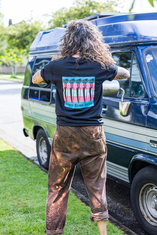 Person wearing a black t-shirt with a colorful graphic on the back, standing in front of a blue van.